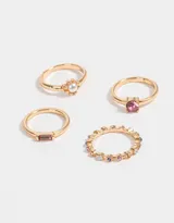 Set de cuatro anillos dorados con diferentes diseños: uno con una perla central, otro con una piedra rosa, otro con strass multicolor y otro con una piedra rectangular rosa.