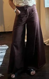 Pantalón ancho de tiro alto, color marrón oscuro o vino, con costuras contrastantes claras. Presenta un calce muy holgado y amplio en las piernas.