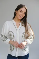 Camisa blanca de manga larga con elástico en puños, cuello mao con botones en la parte delantera y bordados florales en verde.