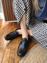 Mocasines de cuero negro con cordones finos y suela plana.