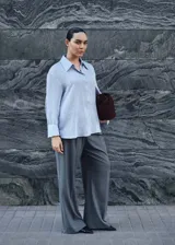 Camisa celeste con rayas verticales finas, de tejido fluido, manga larga abotonada, cuello camisero y corte recto.