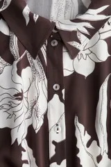 Vestido midi camisero color marrón con estampado floral blanco, cuello camisero, botonadura frontal y mangas cortas. Incluye cinturón extraíble para atar.