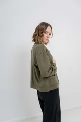 Chaqueta color beige de corte recto, estilo camisa, confeccionada en gamuza con elastano. Presenta cuello camisero, cierre frontal con botones metálicos, bolsillos grandes en el frente y charreteras en los hombros.