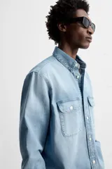 Camisa celeste de denim de algodón, corte relaxed fit, con cuello solapa, manga larga con puños abotonados, dos bolsillos de parche con solapa en el pecho, efecto lavado y cierre frontal abotonado.