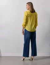 Blusa blanca de gasa marca Zac & Rachel, con cuello a la base, escote en V, abertura central con botones, bolsillo aplicado en el pecho y mangas largas regulables con presilla y botón. Tiene terminación opcional de nudo en el ruedo.