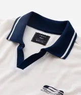 Remera de manga corta con cuello polo contrastante en azul marino y abertura en V. El cuerpo de la prenda es color crema y lleva un estampado frontal con la palabra "WONDER".