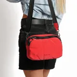 Bandolera roja con correa larga negra regulable, cierre superior con doble cremallera y logo Korium en el frente.