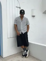 Camisa tejida a rayas verticales blancas y negras, de manga corta y cuello solapa.