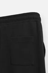 Pantalón negro de corte recto confeccionado en tejido interlock de algodón con elasticidad. Tiene cintura elástica ajustable con cordón, bolsillos frontales y bolsillos traseros de vivo.