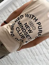 Musculosa de color beige con cuello redondo y corte holgado. Presenta un estampado minimalista en negro en el lateral del pecho con el nombre de la marca Osten Studio y coordenadas geográficas.