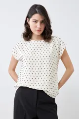 Blusa color crudo con estampado de puntos negros, de corte recto y manga corta.