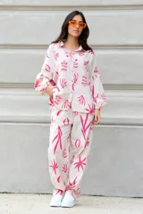 Conjunto de camisa de manga larga y pantalón largo, ambos con estampado abstracto en tonos rosa sobre fondo blanco. Camisa de corte oversized con cuello clásico y cierre frontal con botones. Pantalón con bolsillos laterales.