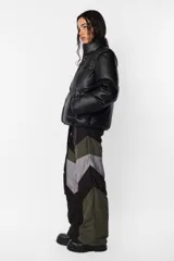 Campera puffer negra de cuerina PU opaca, corte boxy fit, cuello alto con elástico y tancas metálicas, acceso delantero con cierre metálico desmontable y tiracierre de marca, bolsillos ribete con snap metálico y bolsillo superior con cierre metálico cubierto por vista y avío marcario, mangas desmontables por cierre de nylon cubierto con vista, terminaciones de mangas y cintura con elástico interno, forrería al tono, cinta gross estampada nombre de marca y snaps en sus extremos para transportarla al hombro, bolsillo interno de tela base con cierre invisible.