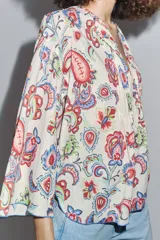 Camisa de algodón color crudo con estampado de cachemir en tonos rojo, azul y verde. Tiene cuello redondo, escote en pico, manga tres cuartos acampanada y bajo asimétrico redondeado.