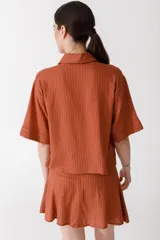 Camisa corta de manga corta color rojo, con doble cartera diagonal con botones de madera, cuello clásico y botamangas marcados. Tiene un bolsillo con aplique de crochet hecho a mano con forma de frutilla.