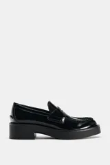 Zapato tipo mocasín de charol negro con detalle de antifaz en el empeine y punta redonda. Suela de 4 cm de altura.