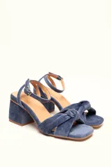 Sandalias de terciopelo azul con taco de 7 cm, tiras anudadas en el empeine y pulsera ajustable al tobillo. La plantilla es extra acolchonada y el forro y la suela son de cuero.