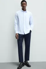 Camisa celeste a rayas verticales blancas, de corte recto, con cuello italiano abierto, mangas largas con puños abotonados y cierre frontal con botones.