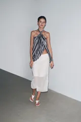 Falda midi color blanco, semitransparente, de tiro medio con cintura elástica, forro corto interior y abertura en la espalda.