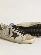 Zapatillas urbanas Golden Goose modelo Super Star, de cuero color blanco con detalles en marrón y beige. Presentan la estrella distintiva de la marca en el lateral, acabado desgastado y suela de goma.