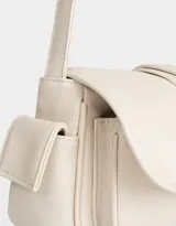 Bandolera color crema de cuerina con solapa con hebilla plateada. Tiene correa regulable con hebilla, cierre con broche a presión y bolsillos laterales con broche a presión.