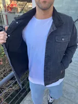 Chaqueta de jean negra con cuello de corderito negro, cierre frontal con botones metálicos, bolsillos con solapa abotonada en el pecho y bolsillos laterales.