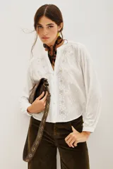 Camisa blanca de manga larga con cuello mao y escote en V. Presenta bordados florales en blanco y dorado en el frente.