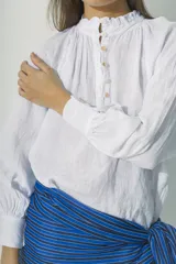 Blusa blanca de lino con cuello fruncido y botones frontales.