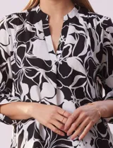 Blusa de gasa estampada con flores rojas y blancas, marca Floral & Ivy. Tiene cuello a la base con escote en V y mangas tres cuartos regulables con presilla y botón.