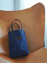 Bolso matero de lona color azul con detalles en cuero marrón, con asas cortas y logo de la marca en cuero.