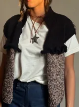 Chaleco tejido de punto con cuello alto, color negro en la parte superior y beige con motas negras en la parte inferior.