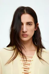 Blusa color crema de gasa con escote en V y cordones cruzados. Tiene mangas largas acampanadas y pliegues en la cintura.