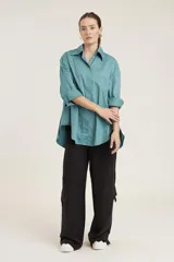 Camisa blanca de corte clásico con cuello abotonado, cierre frontal con botones y mangas largas con puños abotonados. Presenta pequeños apliques de strass plateados dispersos por toda la prenda.