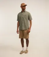 Camisa de hombre de corte relajado, color crudo, con cuello inglés, mangas cortas, abotonado delantero, bolsillo en el pecho y etiqueta de la marca.