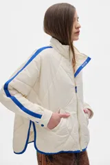 Campera acolchada color crema con cierre frontal y cuello alto. Presenta dos franjas azules en las mangas y ribete azul en el cuello y ruedo.