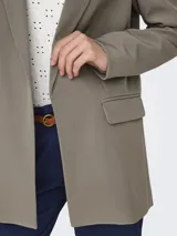 Blazer largo color marrón topo, de corte holgado y tejido sastrero con trama twill. Tiene cuello con solapa y bolsillos delanteros funcionales.