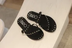 Sandalias negras con tachas plateadas, tira delantera y tira con hebilla al tobillo.