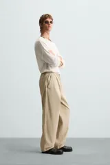 Pantalón de algodón color beige con efecto lavado, corte relajado y pierna ancha. Presenta cintura elástica con ajuste de cordón y cierre frontal con botón, además de bolsillos delanteros y bolsillos traseros de plastrón.