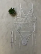 Conjunto de lencería blanco de encaje elastizado, compuesto por un corpiño triangular con breteles regulables, una tanga regulable con portaligas y ligas incluidas.