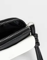 Monedero pequeño de cuerina bicolor, negro y blanco, con bolsillo frontal con broche y cierre superior con tirador de cordón. Incluye correa fina para colgar.