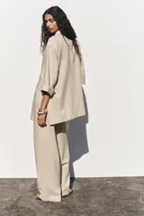 Pantalón color beige de lino, de tiro alto con cintura elástica, bolsillos laterales ocultos en costura y pernera ancha.