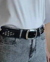 Cinto marrón de cuero con tachas plateadas y doradas, y hebilla metálica rectangular color bronce.