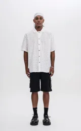 Camisa blanca con textura y botones marrones, de corte holgado y mangas cortas.