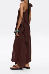 Vestido largo marrón de lino, con corte ajustado y fruncido. Presenta escote de un solo hombro con lazo y maxitira de tejido. Cierre con cremallera invisible lateral y pañuelos laterales.