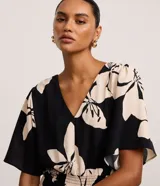 Vestido evasé midi de airflow negro con estampado de flores color crema, escote en V, sisa alargada, mangas cortas amplias y lastex en la cintura.