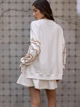 Buzo de algodón color blanco roto, de corte holgado, con puños y tajos laterales. Presenta un bordado artesanal en relieve de líneas orgánicas en color marrón caramelo sobre las mangas.