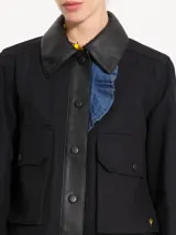 Chaqueta corta negra de gabardina combinada con cuero, con recortes delanteros, bolsillos plaqué con tapa y broches forrados. Presenta volados en denim.