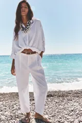 Pantalón blanco de lino, de tiro alto con pinzas delanteras, bolsillos frontales y falsos bolsillos con solapa en la espalda. Incluye cinturón marrón.