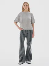 Jean de mujer, tiro medio, corte flare (campana) con estampado de rayas verticales en tonos gris oscuro y verde grisáceo. Confeccionado en denim 100% algodón.