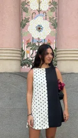 Vestido corto sin mangas, con escote recto y corte a la rodilla. Presenta un diseño bicolor, con un lado blanco con lunares negros y otro lado negro liso.